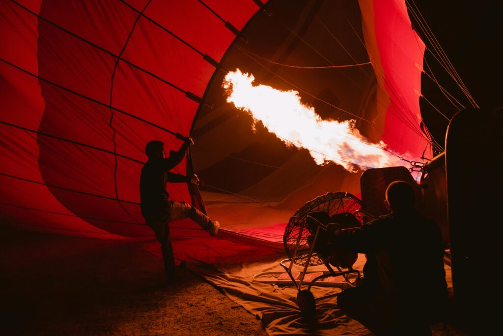 Silhouettes inflating a hot air balloon with flames at dawn in Cappadocia, Turkey.